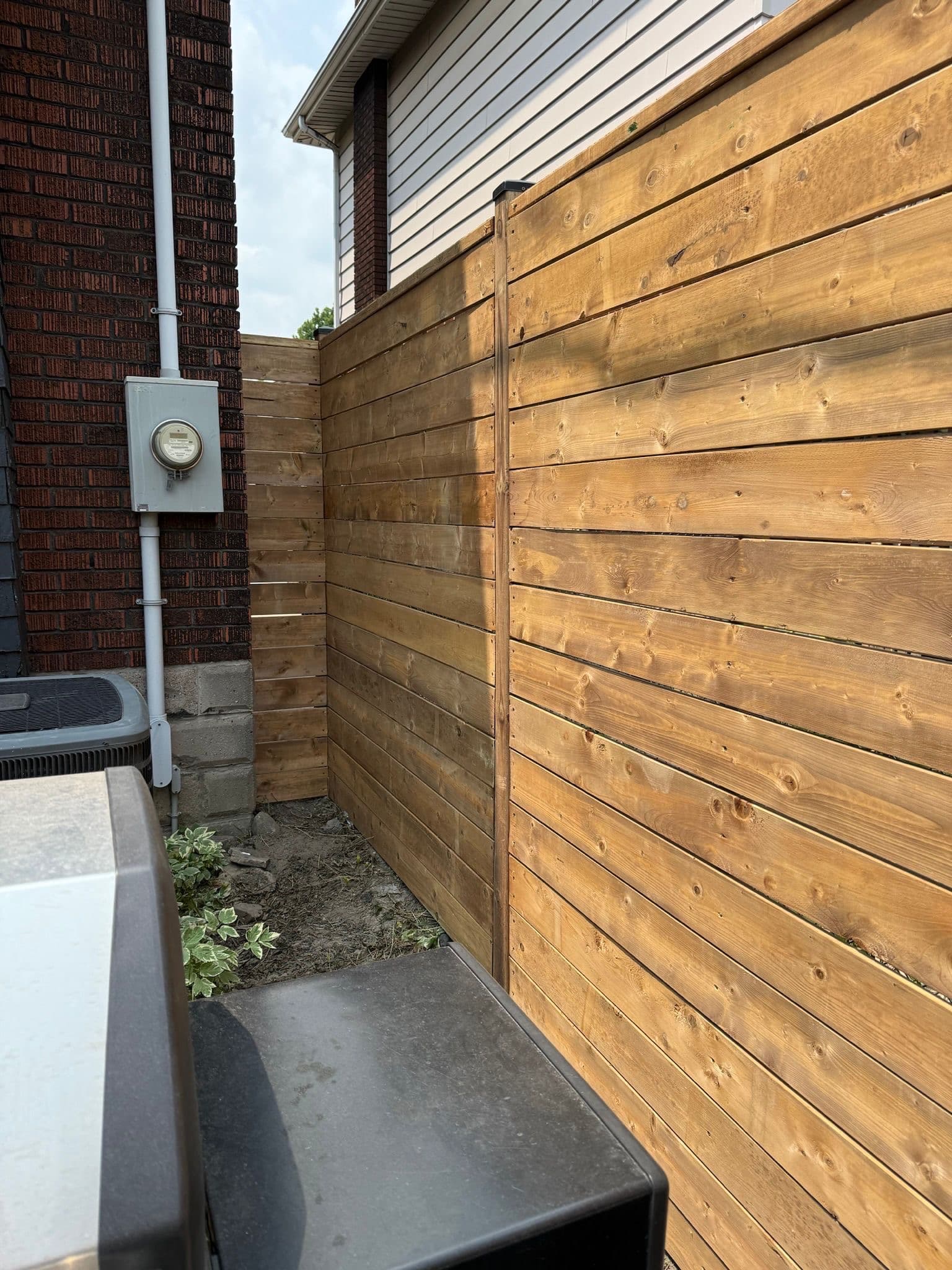 Modern horizontal board wood fence next to brick and siding home